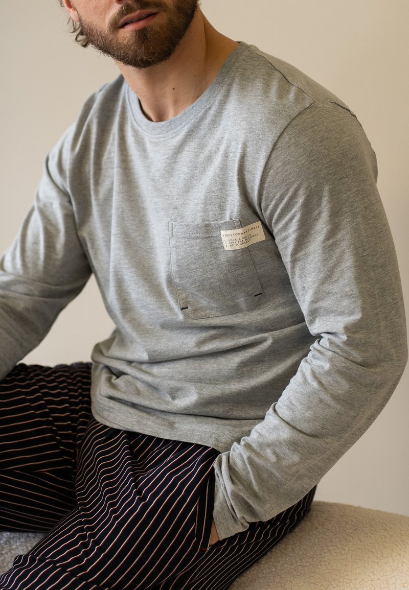 Grijze lange mouwen shirt met een zak en label detail. Gecombineerd met zwart-rood gestreepte broek. Zachte stof met een ontspannen pasvorm.