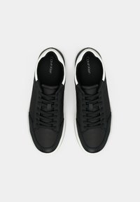 Zwarte sneakers met een gestructureerde bovenkant, witte accenten en platte veters. Heeft een soepele leren neus en een gevoerde binnenzool voor comfort.
