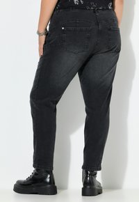 Zwarte denim broek met een ontspannen pasvorm, voorzien van twee achterzakken, subtiele stikdetails en gecombineerd met zwarte veterschoenen.