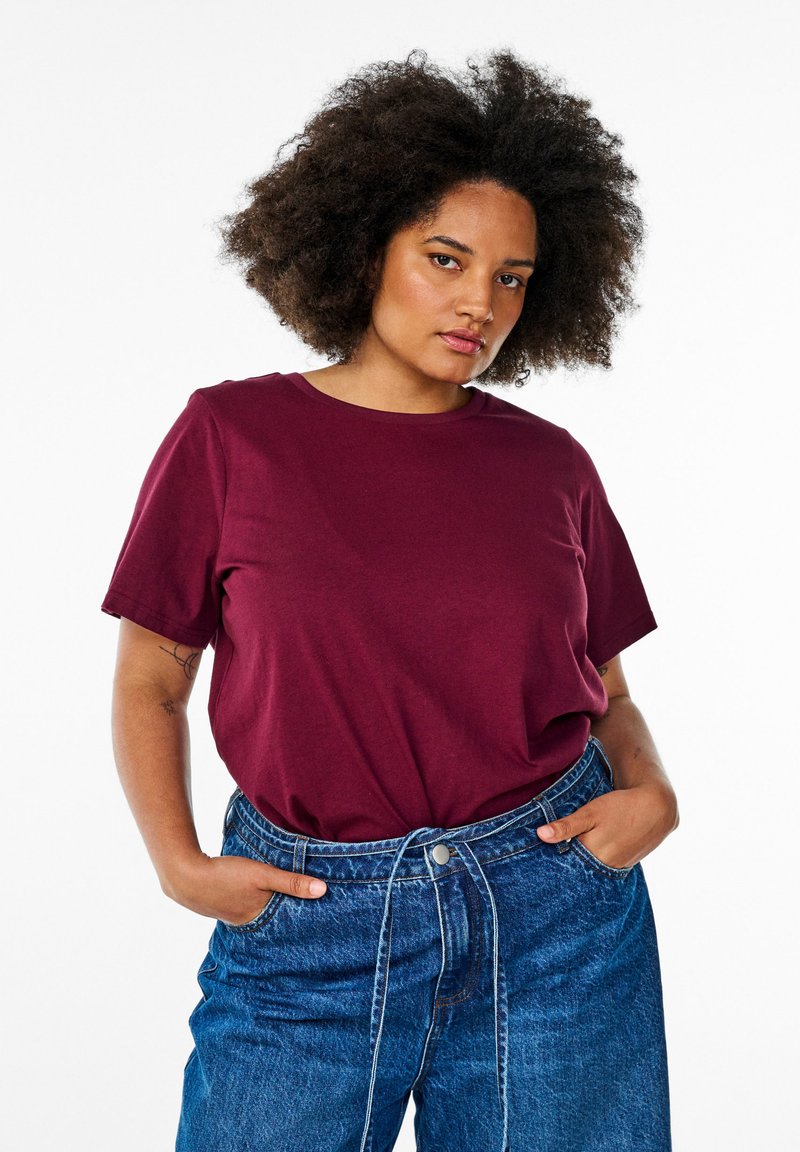 Bordeaux bomulds t-shirt med korte ærmer og rund halsudskæring, parret med løse blå denimbukser med snoretræk i taljen.