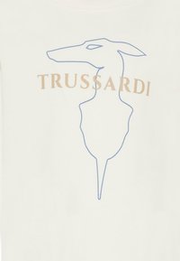 T-shirt blanc présentant une silhouette de chien en contour bleu avec le nom de la marque "TRUSSARDI" en doré au-dessus. Texture lisse, design décontracté.