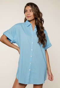 Jasnoniebieska koszula z krótkim rękawem zapinana na guziki, z pionowym wzorem w paski, luźnym krojem oraz miękkim materiałem, z łatwo regulowanym kołnierzykiem.