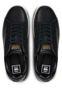 Black leather sneakers with a smooth finish, featuring flat laces, padded collar, and contrasting white rubber soles. Gold logo on the tongue.