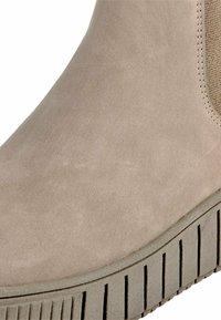 Bottine en suede beige avec panneau latéral texturé, dotée d'une semelle en caoutchouc épaisse avec des rainures verticales pour une traction et une stabilité optimales.