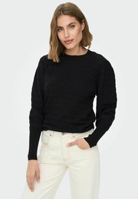 Svart teksturert genser med lange ermer og rund hals, kombinert med lysfargede jeans; glatt strikket stoff og ribbede mansjetter.