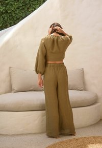 Olivgrünes Leinen-Crop-Top mit Puffärmeln, kombiniert mit passenden weiten Hosen. Weiche Textur, elastischer Bund und entspannter Schnitt.