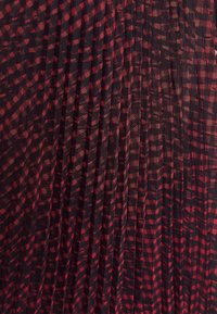 Rød og sort plisseret stof med et ternet mønster, der har en let tekstur og blød fald.