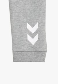 Grijze sweatpants met een zachte textuur en drie witte chevronstrepen nabij de zoom. Het ontwerp is eenvoudig en sportief.