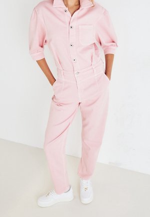 Vaaleanpunainen puuvillahaalari, jossa on lyhyet hihat, etupainike ja tasku. Yhdistetty valkoisiin lenkkareihin, joissa on pyöreä kärki ja litteä pohja.