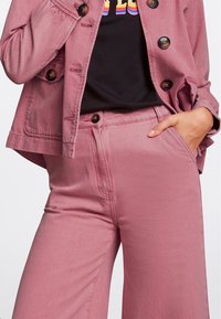 Chaqueta de denim rosa con cierre de botones y bolsillos laterales, combinada con pantalones de pierna ancha de tiro alto en rosa a juego. Camiseta negra debajo.