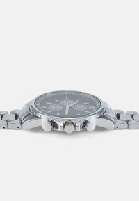 Montre en acier inoxydable argenté avec un cadran noir, trois sous-cadrans et une touche de vert. Chronographe et trois poussoirs sur le côté.