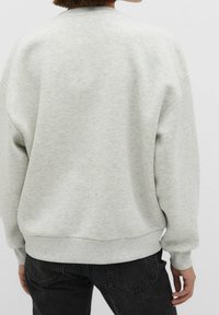 Sudadera gris de ajuste relajado, con cuello y puños acanalados. Textura suave y diseño sencillo. Combinada con jeans oscuros.