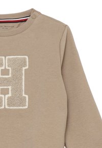 Felpa beige con un logo "H" testurizzato di colore crema. Include un collo a costine con bottoni a pressione e maniche lunghe.