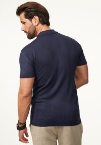 Marineblaues gestricktes Poloshirt mit kurzen Ärmeln und strukturierten vertikalen Streifen. Verfügt über einen klassischen Kragen und eine taillierte Silhouette.