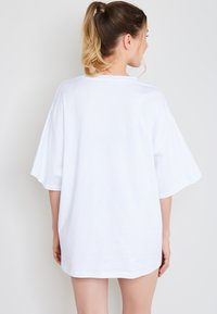 Oversized weißes T-Shirt aus Baumwolle mit kurzen Ärmeln und rundem Ausschnitt, glatter Textur und schlichter Gestaltung.