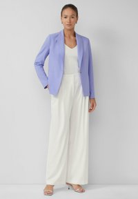 Lavendel blazer met een getailleerde pasvorm en notch lapels, gecombineerd met een witte v-hals shirt en wijde witte broek, afgerond met zilveren haksandalen.