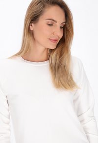 Top alb cu mânecă lungă, cu un guler ribflat și detalii texturate subtile. Material moale, croială lejeră, design minimalist.