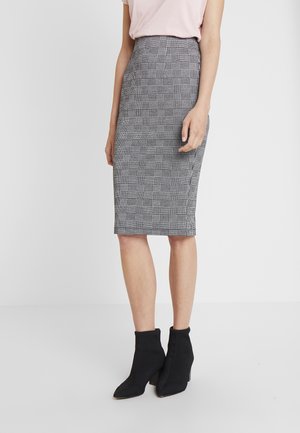 Kobieta ubrana w czarno-białą ołówkową spódnicę w kratę do kolan oraz czarne botki na obcasie na jednolitym tle.