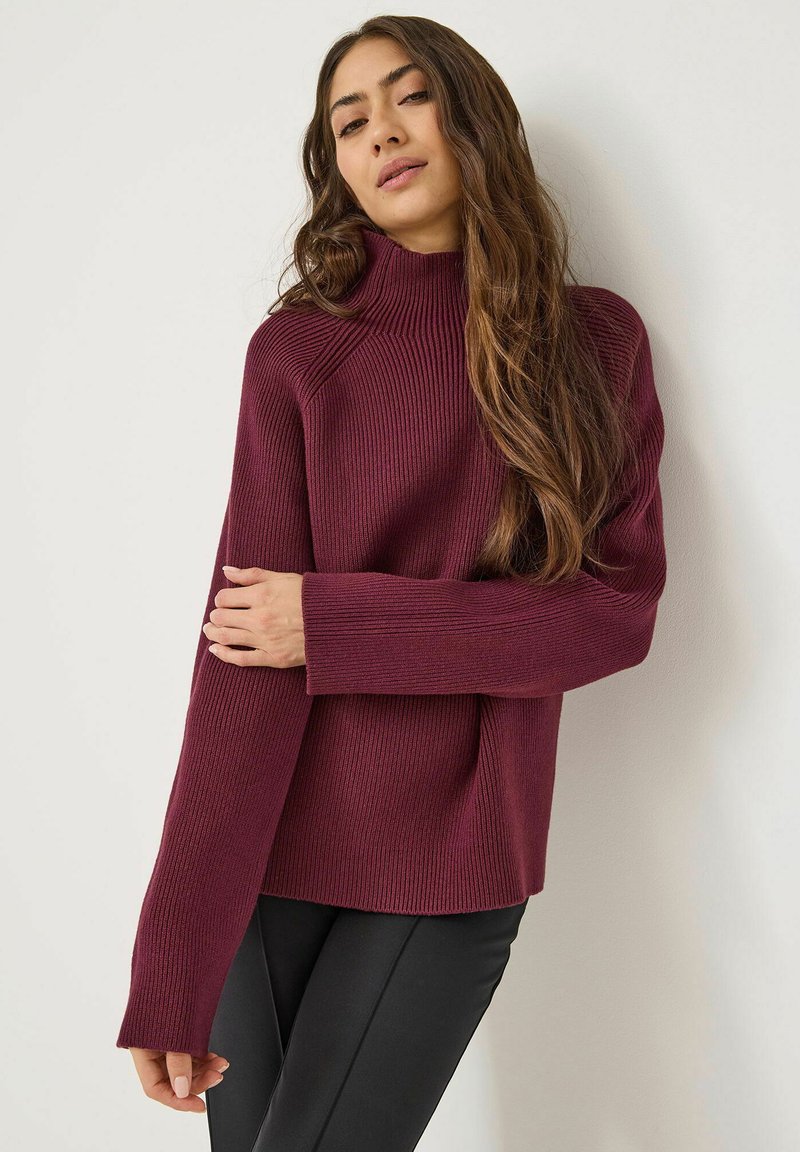 Maglione a collo alto color bordeaux con texture a coste e maniche lunghe, caratterizzato da una vestibilità rilassata e spacchi laterali, abbinato a leggings neri.