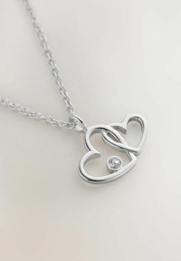 Ciondolo a forma di cuore in argento su una catena, con due cuori intrecciati e una piccola gemma trasparente. Texture liscia con finitura lucida.