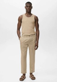Beige tanktop, beige skræddersyede bukser og brune sandaler. Enkel design, tætsiddende pasform, glat tekstur og flad front med sidelommer.