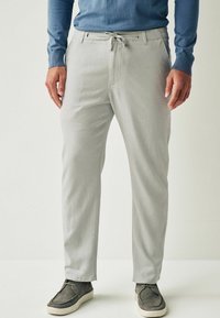 Pantalons gris clair avec une texture lisse, dotés d'une taille à cordon de serrage et de poches avant, associés à des chaussures décontractées gris foncé.