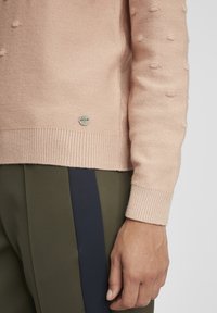 Pull en tricot rose clair avec un design en relief de bobbles, poignets et ourlet côtelés, associé à un pantalon vert olive avec des rayures navy sur les côtés.