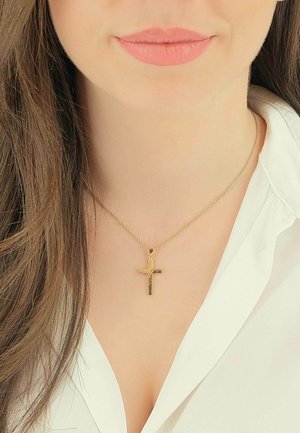 Collana con pendente a croce d'oro su una catena sottile, caratterizzata da una finitura lucida con incisioni lineari, indossata sopra una camicia bianca con colletto.