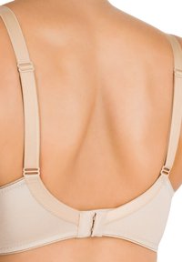 Reggiseno beige con spalline regolabili, texture liscia e chiusura a gancio. Presenta un design sagomato per il supporto con una finitura senza cuciture.