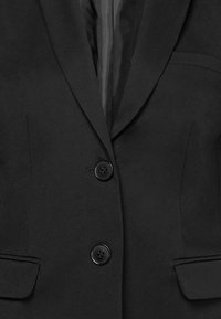 Svart kavaj med slagkrage, två framknappar, sidofickor och en mjuk tygtextur.