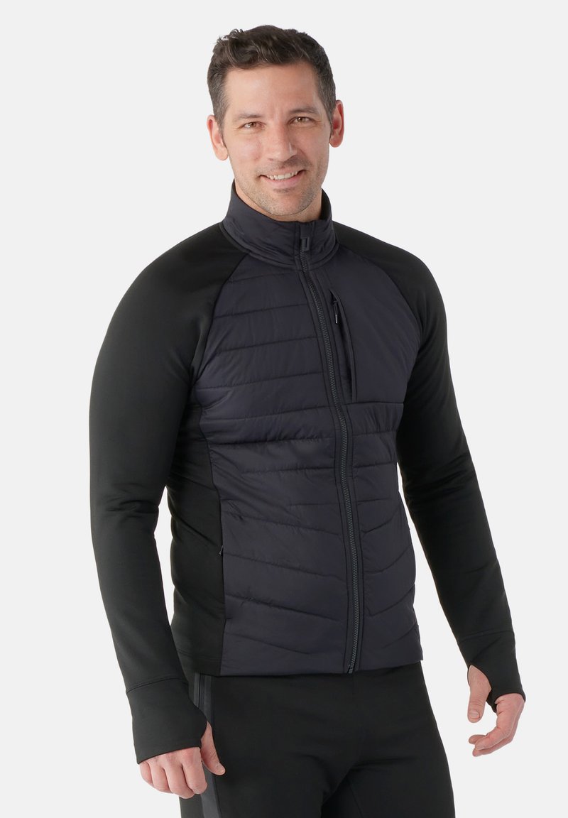 Sort softshell jakke med quiltet front, tætsiddende design, høj krave og lynlåslommer. Glat tekstur på ærmer og sider.