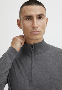 Gray zip-up sweater with a high collar, ribbed cuffs, and a smooth texture. The zipper is positioned centrally on the front.
