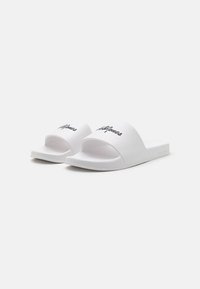 Baltos šlepetės turi plačią juostą su "Jack & Jones" juodu užrašu, tekstūruotu padu ir paprastu, minimalistiniu dizainu.