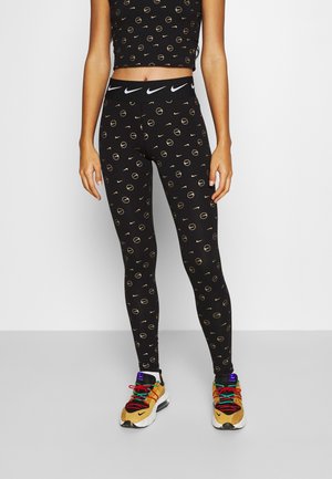 Un crop top noir et des leggings avec un motif circulaire doré ; les leggings présentent une taille noire avec un logo Nike blanc ; des chaussures de sport colorées.