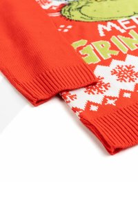 Maglione rosso a maglia con un motivo di fiocchi di neve bianchi e un design di personaggio verde. I polsini sono a coste e il tessuto appare texturizzato.
