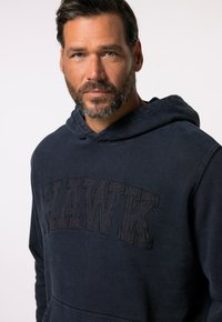 Námořnická modrá mikina s velkým nápisem "HAWK" v texturovaném provedení. Obsahuje kapuci se stahovací šňůrkou a přední kapsu. Měkký bavlněný materiál.