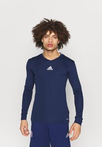 Marine langærmet træningsskjorte med V-halsdesign, der har Adidas-logoet i hvidt i midten. Glat, tætsiddende materiale.