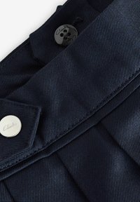 Tessuto blu navy con una trama liscia presenta un design plissettato. Include un bottone nero a quattro buchi e un bottone con il logo Clarks in metallo argentato.