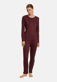 Bordeaux långärmad topp och matchande byxor, tillverkade av mjukt tyg med en slät yta. Har rund halsringning och figurnära design.