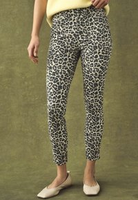 Leopard print leggings in cream and black, slim fit, ankle-length, with a smooth texture and standard waistband. Paired with light flats.