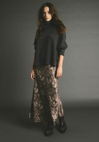 Mørkegrå, chunky turtleneck sweater parret med en lang, mønstret slangeskindsrabat i jordfarver, suppleret med sorte hælede støvler.