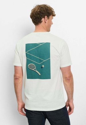 Mann trägt weißes T-Shirt mit Tennisplatz-Grafik, Schläger und Ball auf der Rückseite, steht vor einem schlichten weißen Hintergrund.