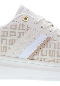 Valkoiset sneakerit, joissa on teksturoitu päällinen, toistuva logokuosi, beige sivuakkentit ja valkoinen nahkakaista, viimestelty kultaisilla reikillä.