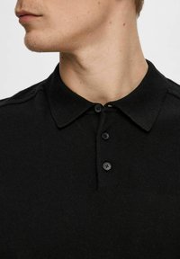 Svart polo-skjorte laget av strukturert strikket stoff, med en klassisk krage, tre svarte knapper og subtile skulderdetaljer.