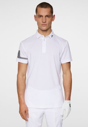 Weißes Poloshirt mit strukturierter Oberfläche, zwei Knöpfen und einem schwarzen Logo am Kragen. Der linke Ärmel hat ein schwarz-weißes gestreiftes Design.