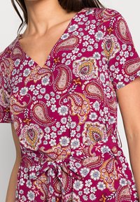 Fuchsiové šaty s V-výstřihem, krátkými rukávy a zavazováním v pase. Po celém povrchu květinové a paisley vzory v bílé, oranžové a fialové barvě.