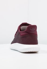 Sportovní bota v barvě bordo s texturovaným pleteným svrškem, bílou polstrovanou podrážkou a zesílenou patou s nenápadným logem.