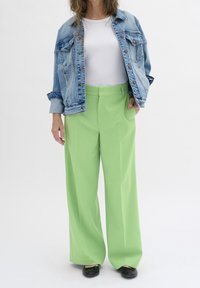 Lichtblauwe denimjack, witte geribde tanktop en wijdvallende, limoen groene broek. Zwarte schoenen met een decoratieve randafwerking.