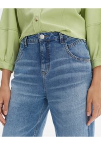 Light blue denim high-waisted jeans with a slight stretch, featuring five pockets, a button closure, and subtle fading across the fabric.