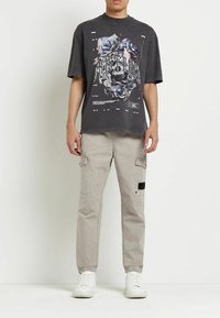 Camiseta gráfica de gran tamaño en color gris con diseño floral y texto, combinada con pantalones cargo grises claros con bolsillos y puños elásticos, usados con zapatillas blancas.
